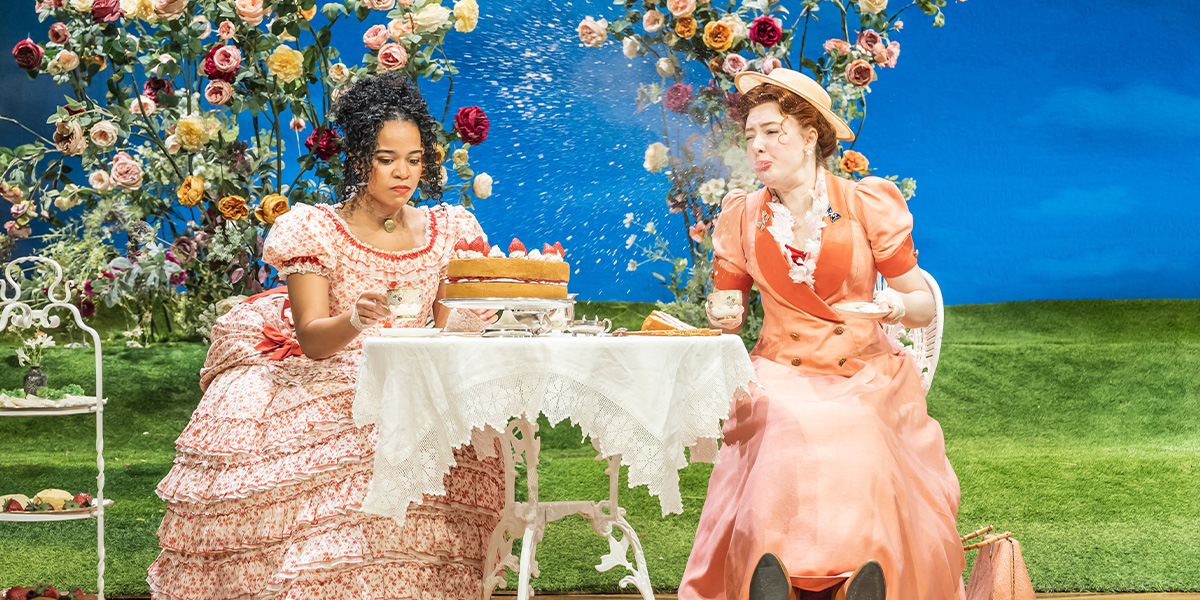 Jessica Whitehurst and Kitty Hawthorne in elegant costumes, smiling, on stage with theatrical lighting and set design.