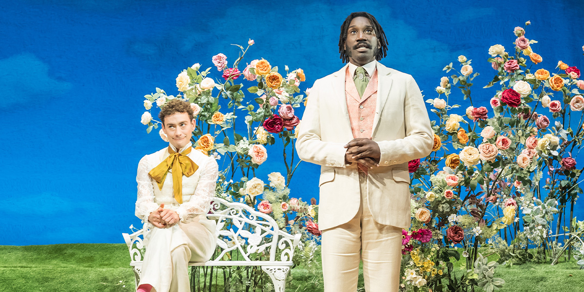 Olly Alexander and Nathan Stewart-Jarrett perform on stage, dressed in period costumes, with a vibrant backdrop.