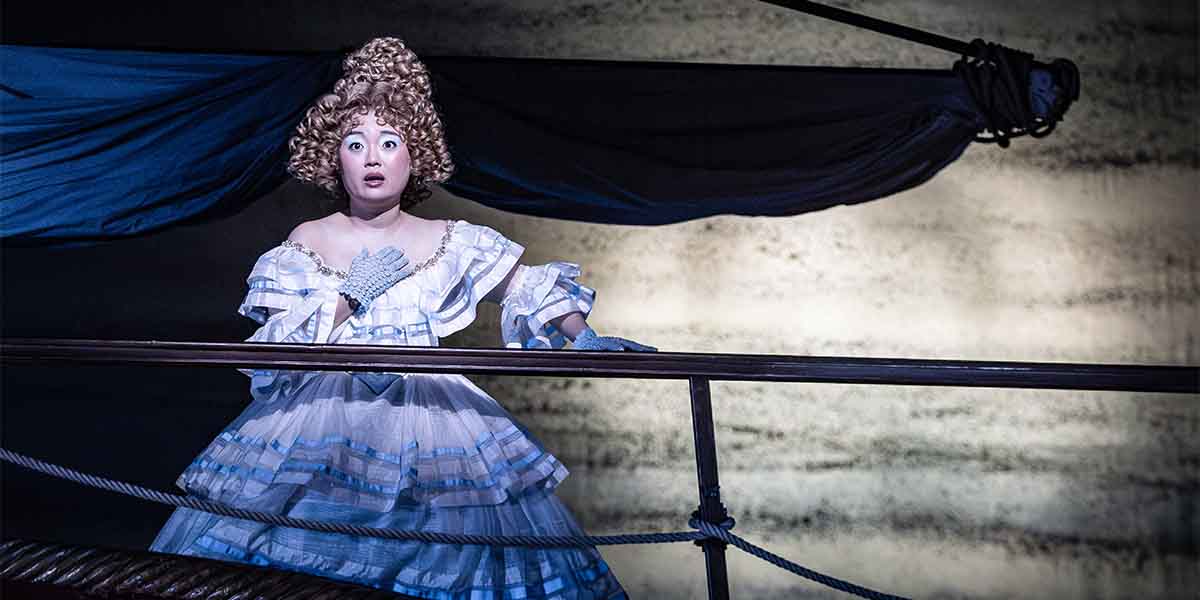 Henna Mun, dressed in a white gown with blue accents, looks surprised while standing on a ship's railing.