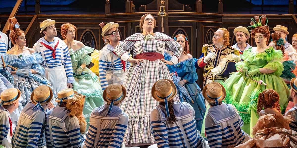 The cast of ENO's HMS Pinafore in period costumes, smiling, with a vibrant stage backdrop.