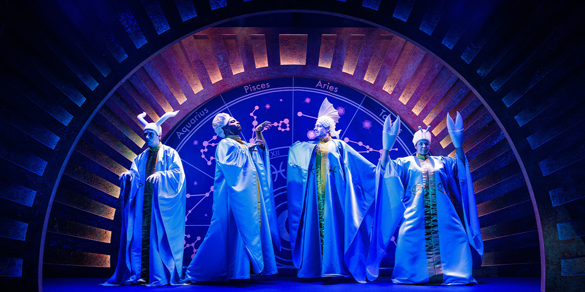The cast of 'Who Let The Gods Out' poses together, smiling, in a brightly lit setting.