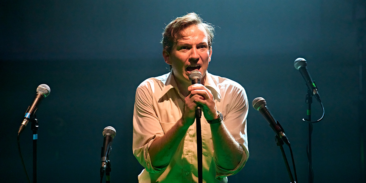 A man in a stylish outfit stands confidently, with a textured background and soft lighting enhancing the scene.