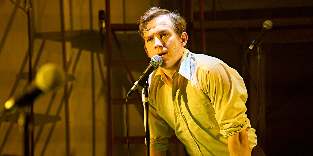 Jack Holden stands confidently in a dramatic pose, wearing a dark costume against a textured backdrop.
