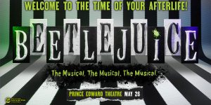Beetlejuice in a striped suit, grinning widely, stands on a stage with vibrant, colourful lighting.