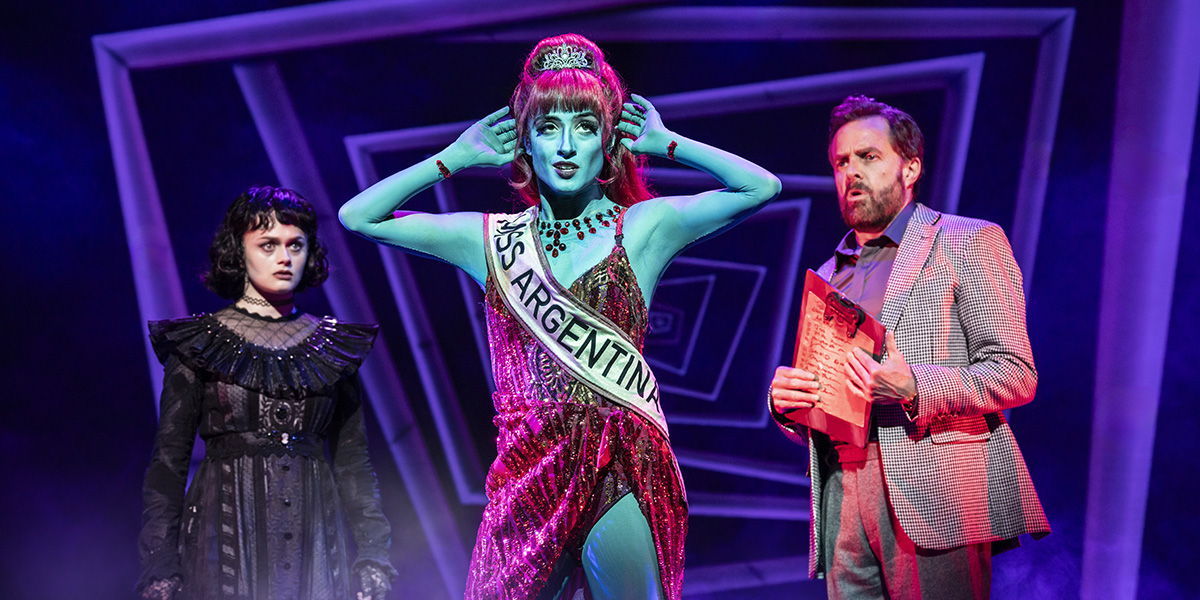 A performer dressed as Beetlejuice, with green and black striped suit, poses dramatically on stage.