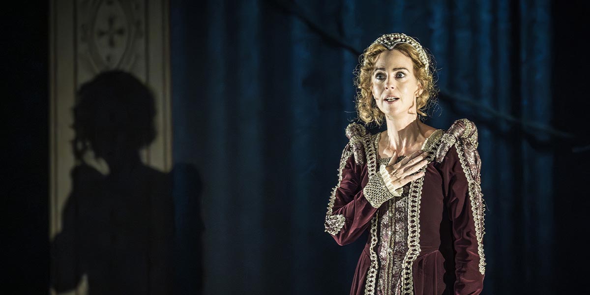 Miranda Raison, dressed in a burgundy gown with intricate detailing, performs passionately on stage.