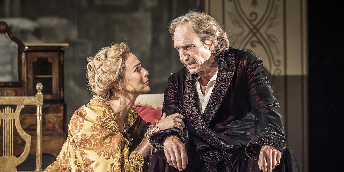 Ralph Fiennes and Miranda Raison pose together, smiling, against a soft, neutral background.