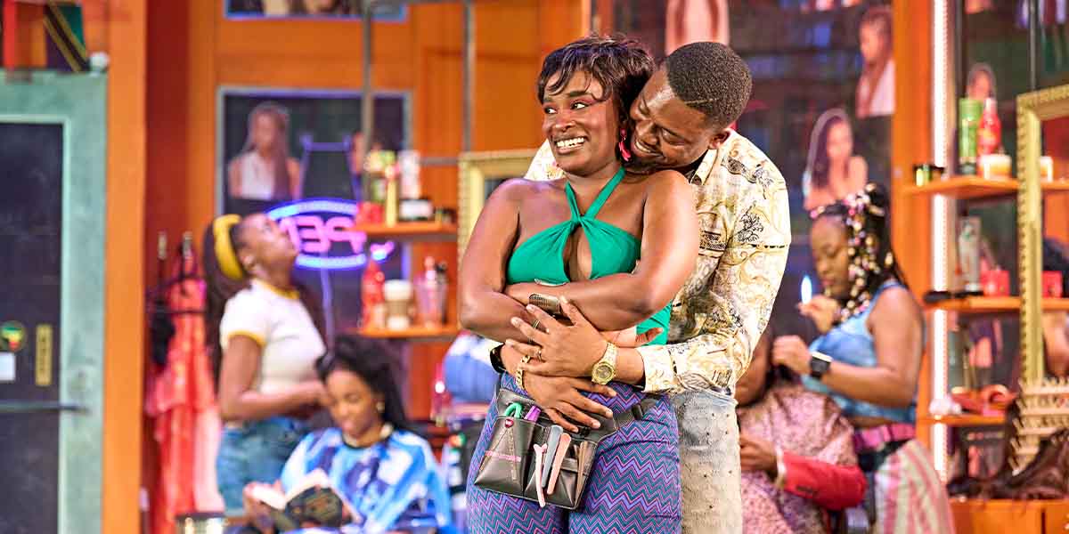 Jajas Sewa Zamba and Karene Peter embrace joyfully, surrounded by vibrant salon decor and other patrons.