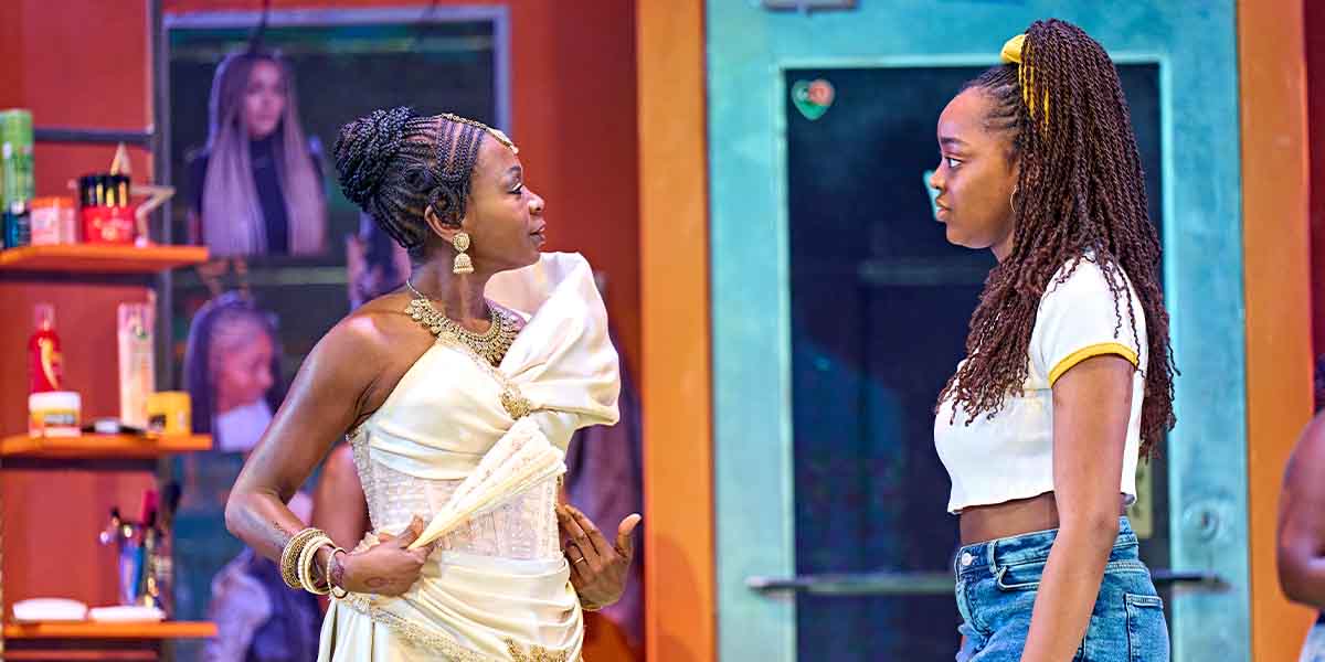 Zainab Jah, dressed in white, gestures while speaking to Sewa Zamba, who wears a cropped top.