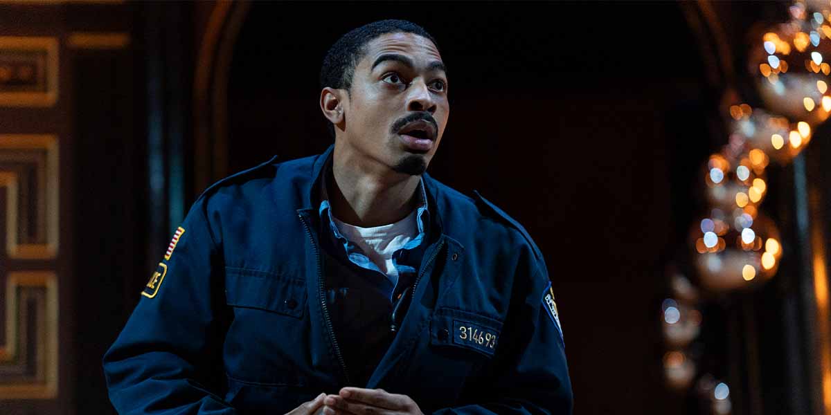 Imani Yahshua as SK Evil, wearing a dark uniform, looks surprised against a softly lit background.