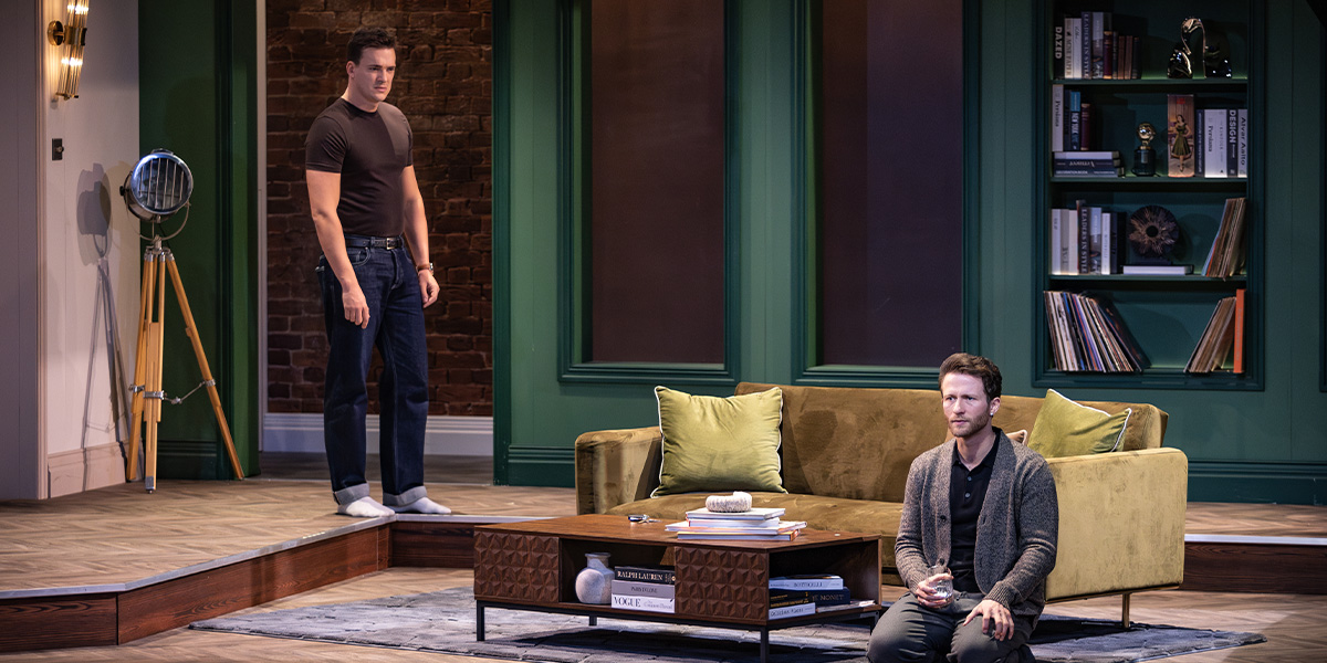 One person sits in an armchair while another stands across the room.