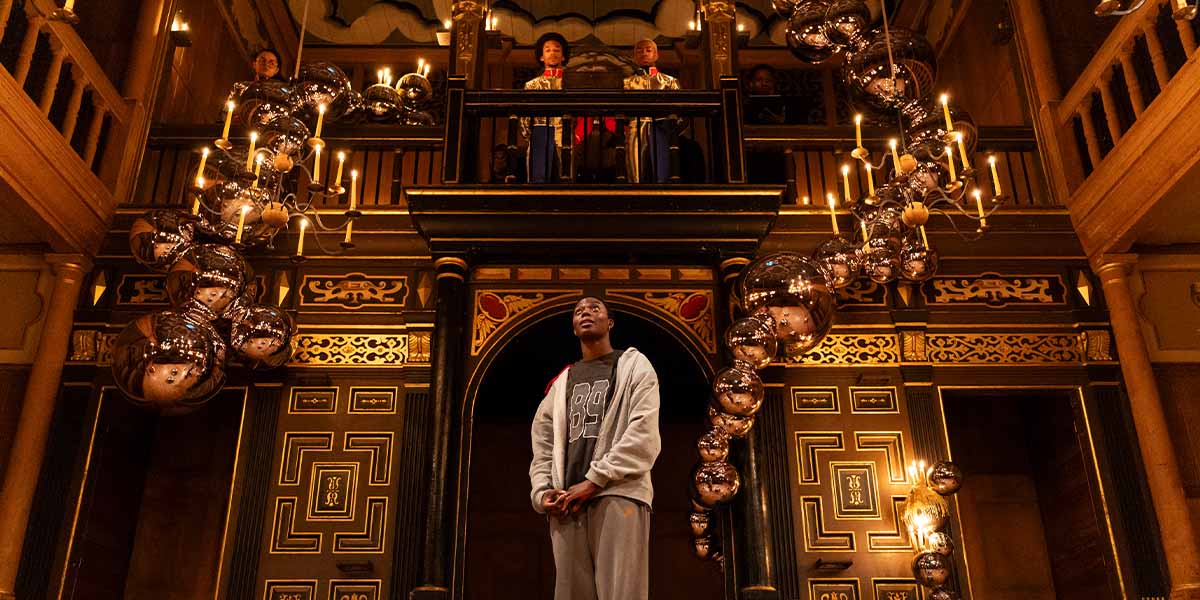 Selina Jones as Azure, wearing a grey costume, performs on stage at Shakespeare's Globe.