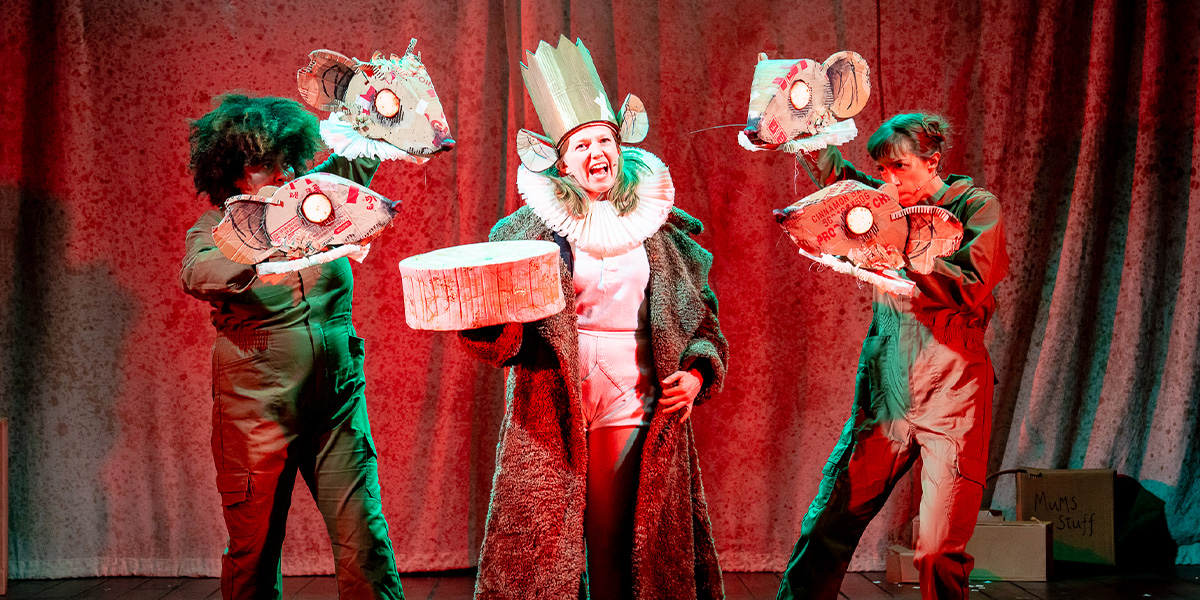 A ballet dancer in a pink tutu performs an arabesque on stage, with a festive backdrop and soft lighting.