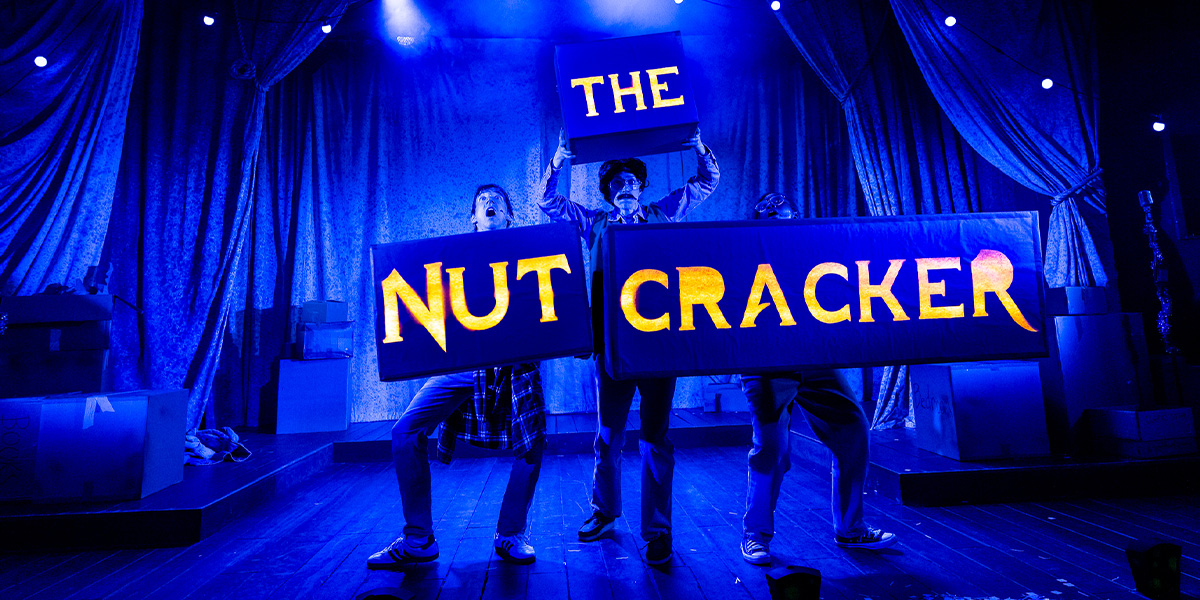 A ballet dancer in a pink tutu performs an arabesque on stage, surrounded by festive decorations and soft lighting.