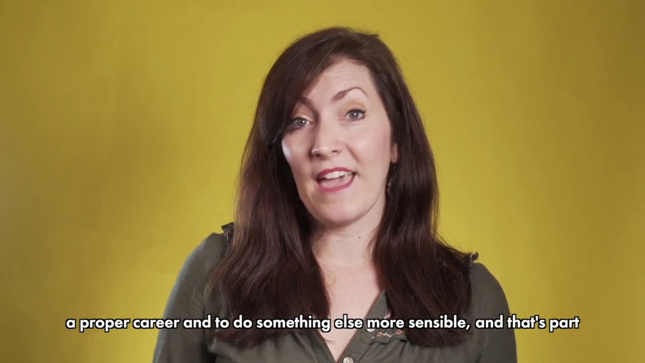 A diverse group of people in a theatre, engaged in discussions, surrounded by stage lights and props.