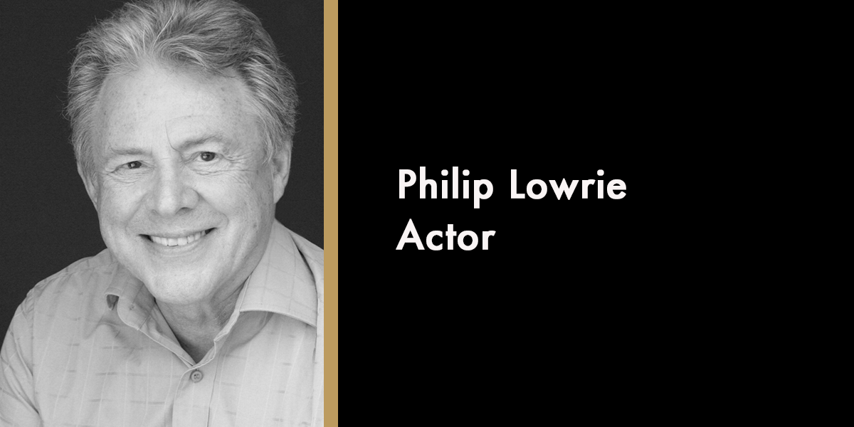 A portrait of Lowrie Philip, smiling, with a dark background and soft lighting highlighting his features.