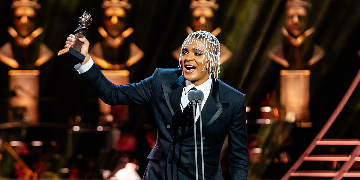 Layton Williams wins Best Actor in a Supporting Role in a Musical for Titanique. Layton holds the Olivier statue up on stage, smiling.