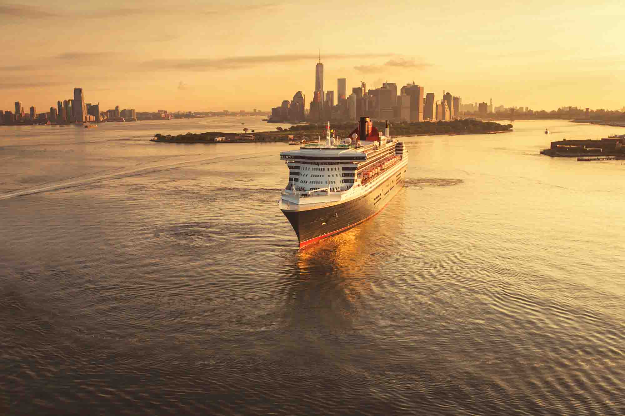A cruise ship sails through calm waters at sunset, with a city skyline silhouetted in the background.