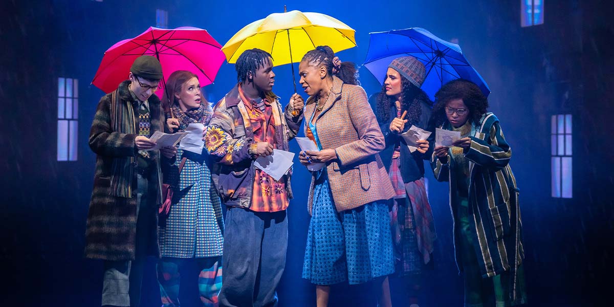 A vibrant scene from Paddington The Musical featuring Paddington Bear in a blue coat and red hat.