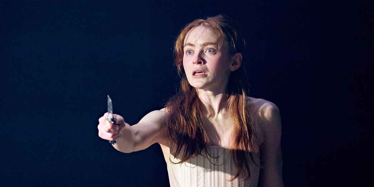 Sadie Sink, in a light dress, holds a knife, looking distressed against a dark background.