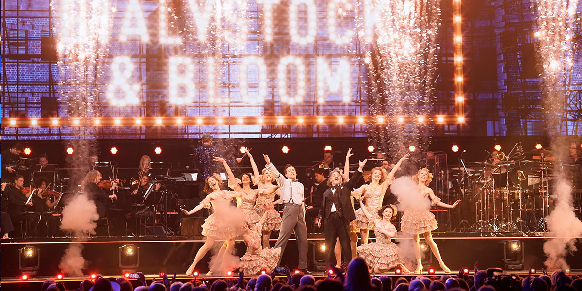 Producers of the Big Night Of Musicals 2026 pose together, smiling, in formal attire against a stage backdrop.