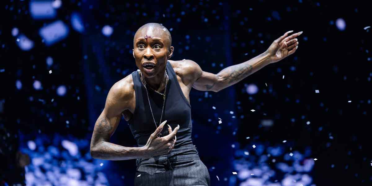 A performer in a sleeveless top gestures expressively, surrounded by falling confetti and dramatic lighting.