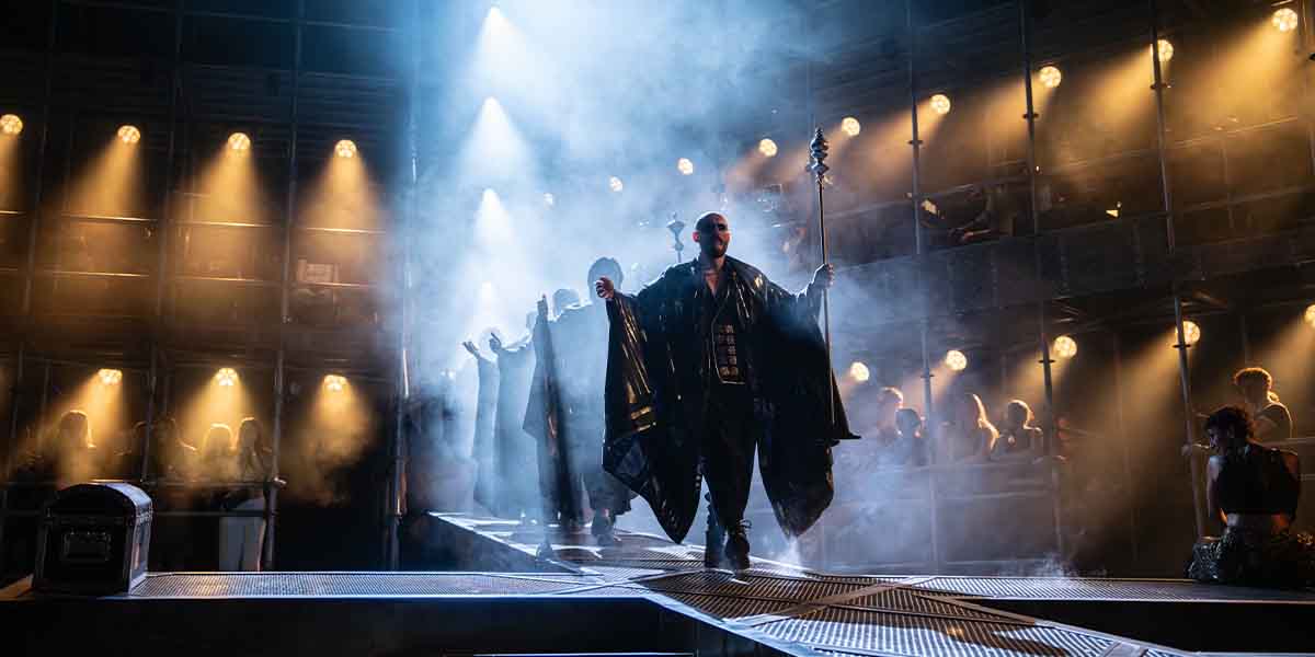 Bob Harms leads a group of performers on stage, shrouded in smoke and dramatic lighting.
