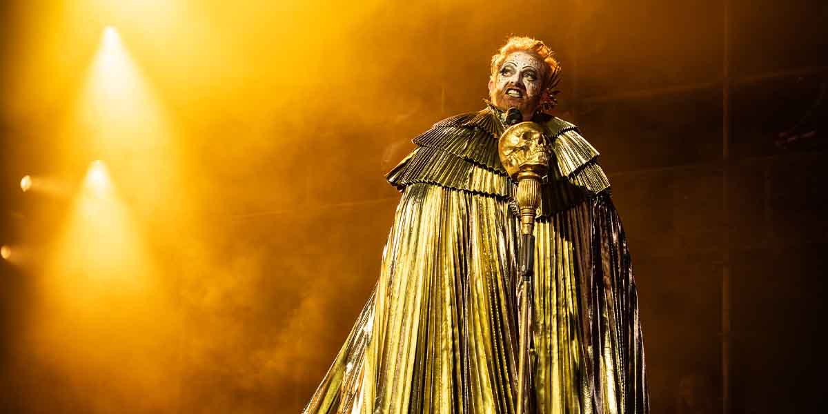 Jesse Tyler Ferguson performs in a dramatic golden costume, illuminated by warm stage lights and smoke.