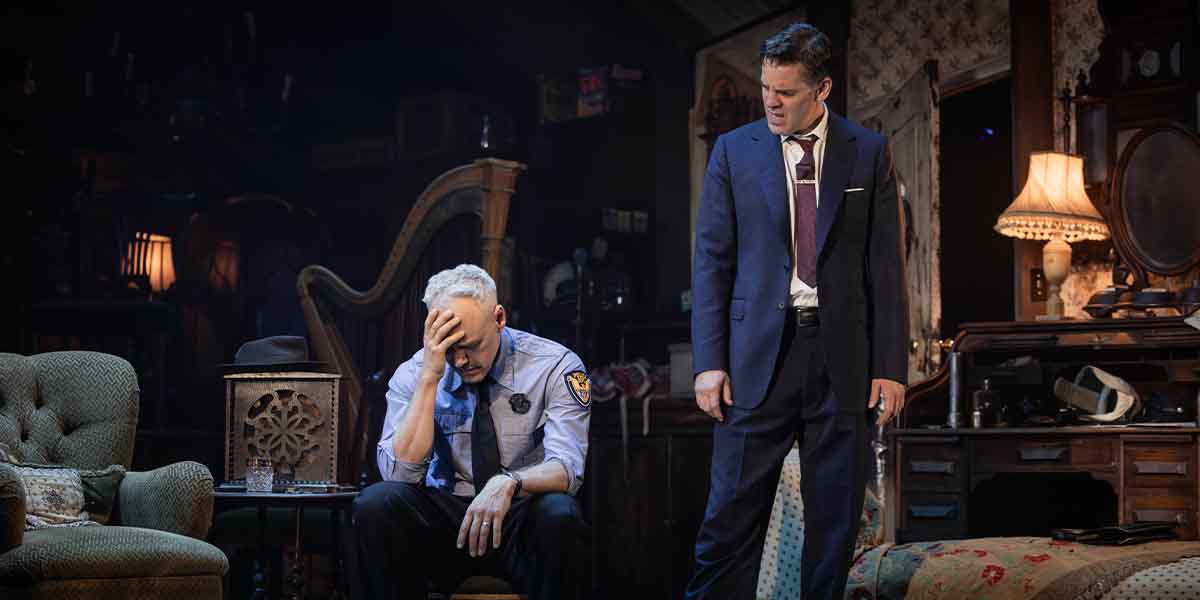 A distressed person in a police uniform sits, while another in a suit stands nearby, concerned.