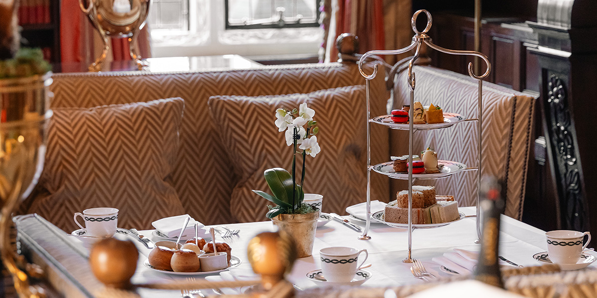 Elegant afternoon tea setup with fine china, pastries, and sandwiches, set against a luxurious hotel backdrop.
