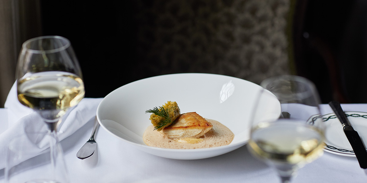 A beautifully plated fish dish garnished with herbs, served in a white bowl on a table setting.