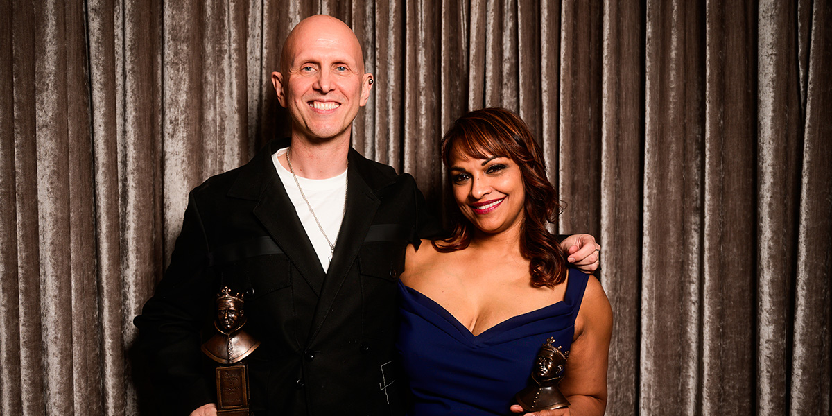 Wayne McGregor and Danielle de Niese pose together, smiling, in formal attire against a neutral background.