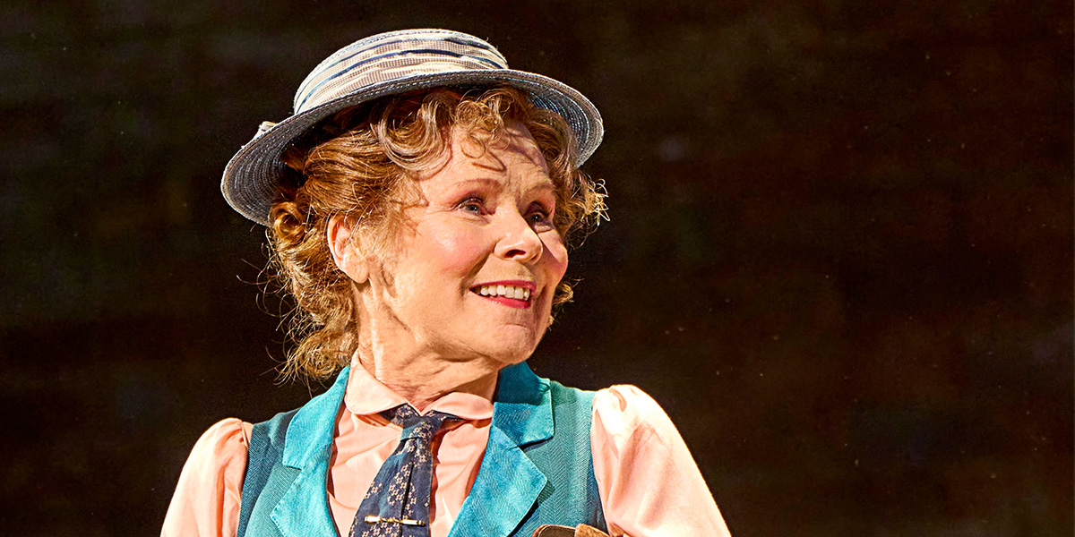 Imelda Staunton smiles while seated, wearing a black top, against a blurred background.