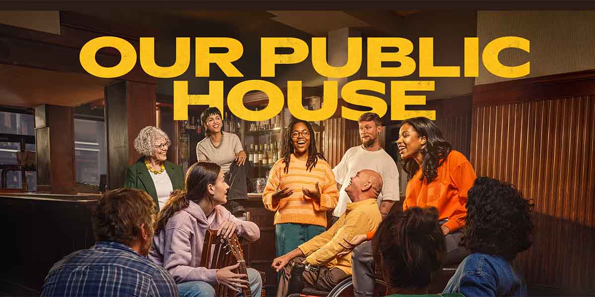 A diverse group of people engaged in conversation, smiling, in a warm, inviting pub setting.