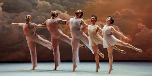 Five dancers in sheer costumes perform gracefully against a backdrop of dramatic clouds.